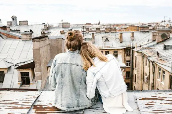A young couple overlooks at their city from a high rooftop while leaning on each other's shoulders. 