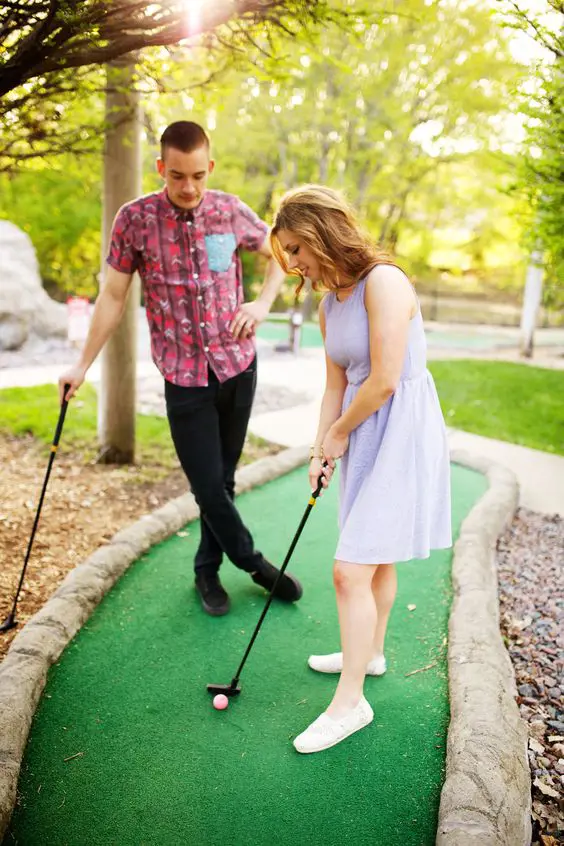 A couple enjoys Mini Golf with black Golf Clubs and pink ball. 