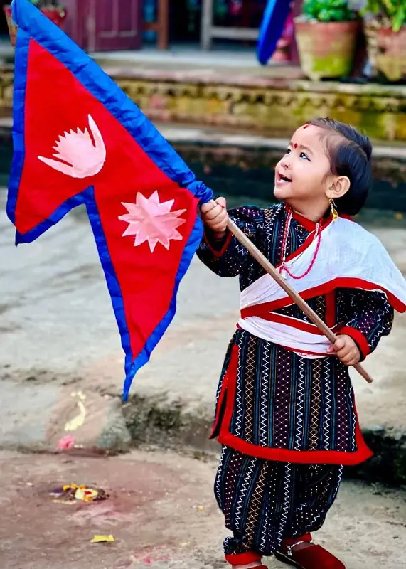 A little girl dresses in cultural outfit waves the Flag of Nepal.