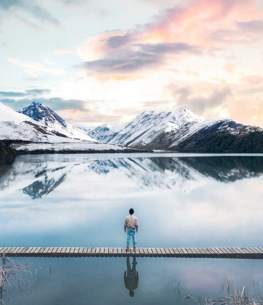 The captivating sight of a person standing on wooden planks across snow capped mountains seen from the back