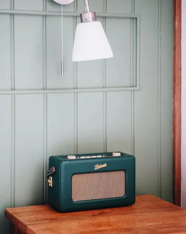 The picture showcases an antique green radio resting on a table accompanied by a hanging lamp