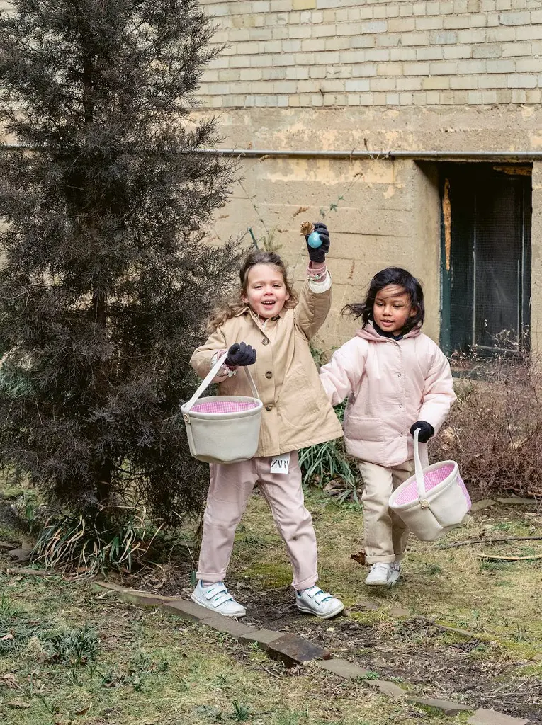 The photo captures girls wearing warm clothes, joyfully participating in an outdoor scavenger hunt holding baskets in their hands, eagerly searching for hidden treasures