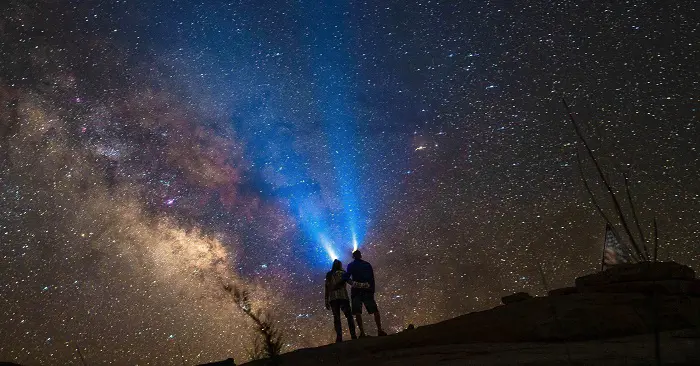 A young pair look at the star studded night sky as they cuddle affectionately. 