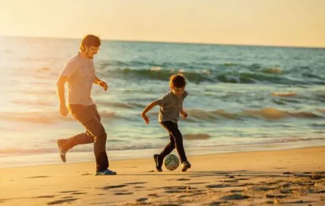 Father and son playing football on the beach