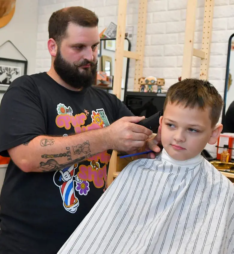 A boy getting is hair trimmed by a bearded hairstylist