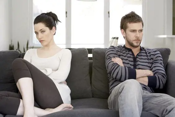 A couple seen ignoring each other while being seated on a couch