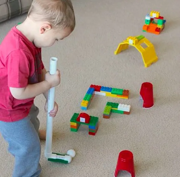 A toddler plays a mini golf with a ping pong ball on a setup created using lego bicks