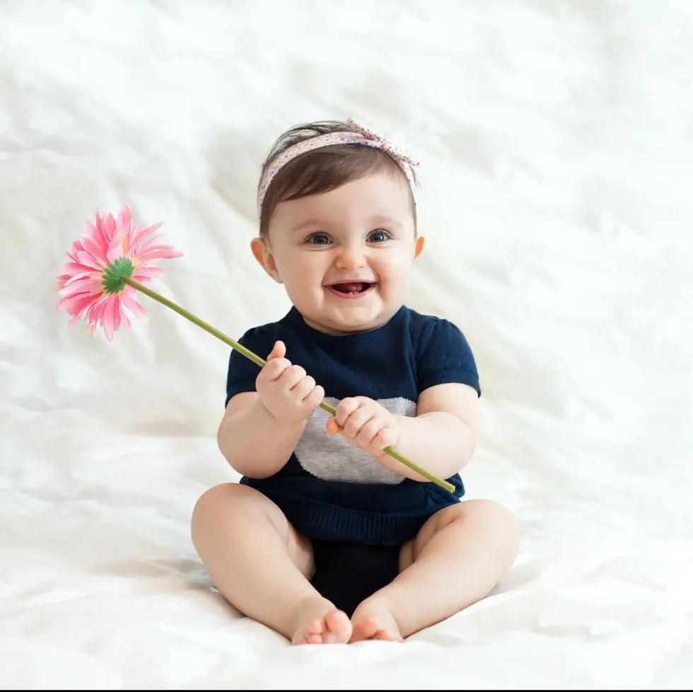 A lovely baby sitting smiling with a flowers on hand