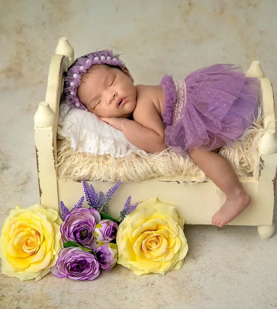 A newborn baby rests peacefully in the bed accompanied by a delicate flowers