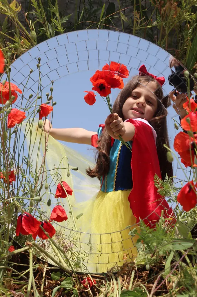 A little girl holds poppy flowers in her hand and their beauty doubled by the glass