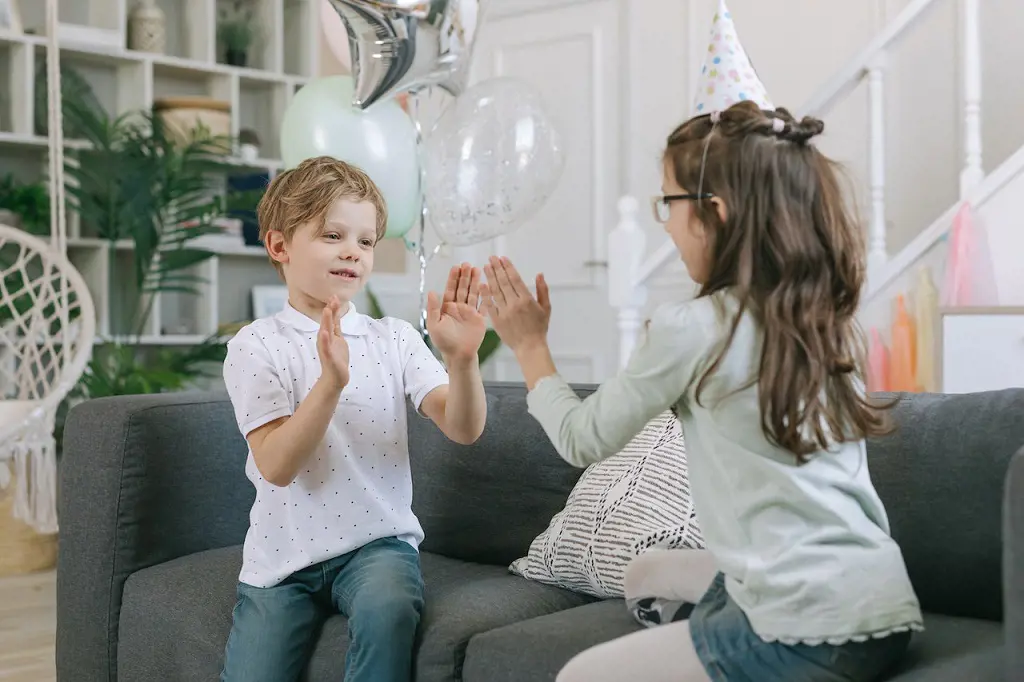 A little boy and a little girl play hand clapping games in their living room.